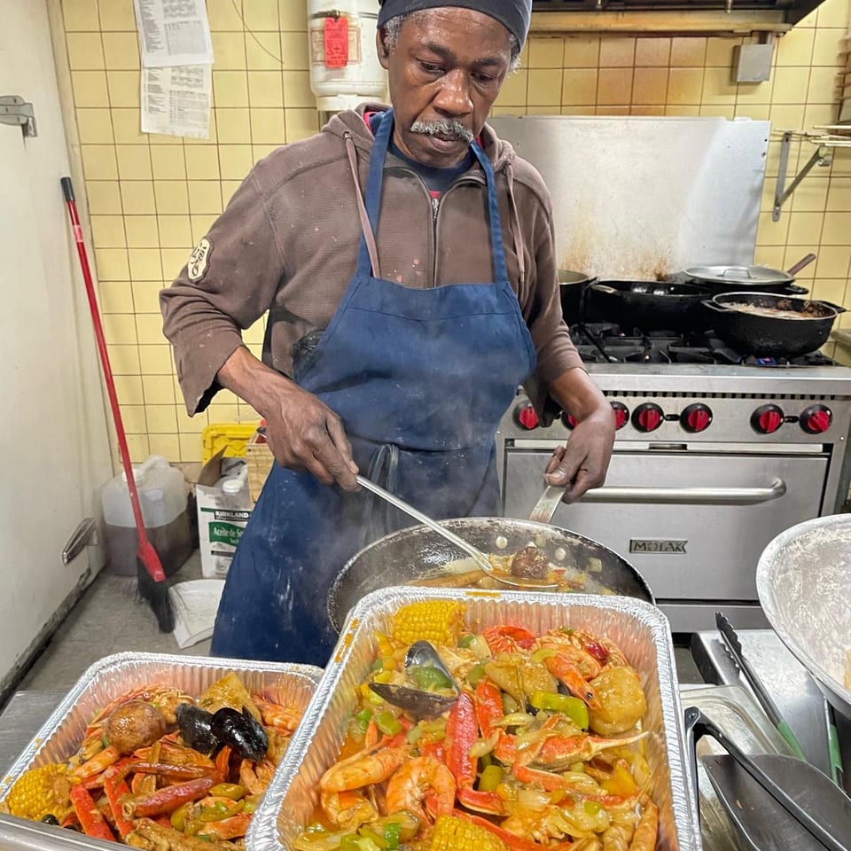 Cook in an apron prepares seafood boil with shrimp, crab, sausage, vegetables, and corn in a restaurant kitchen.