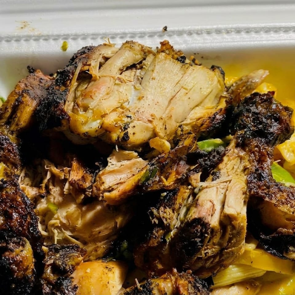 Open takeout container filled with charred grilled chicken pieces, yellow rice, and green pepper garnish.