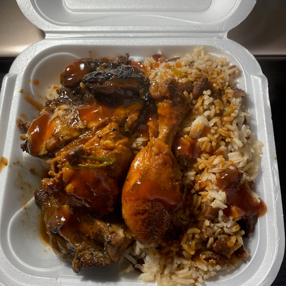 Takeout container filled with saucy grilled and fried chicken pieces alongside seasoned rice and beans.