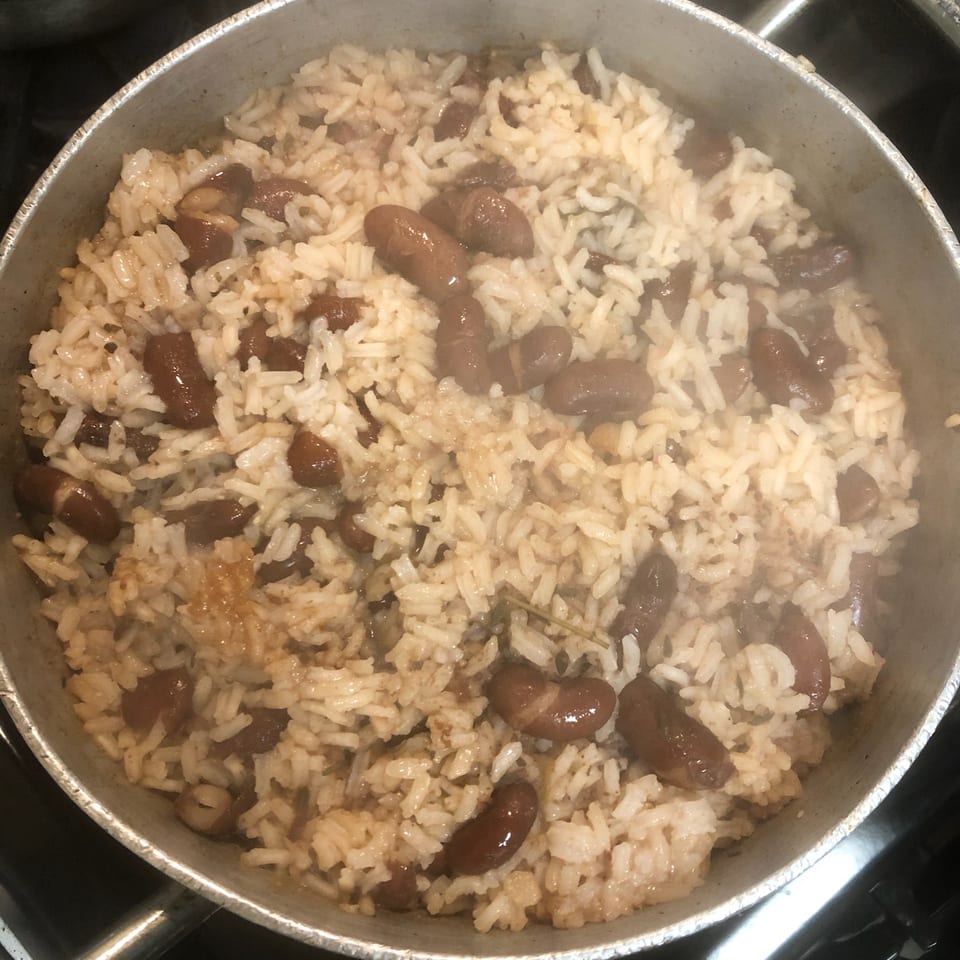 Steaming pot of white rice mixed with red kidney beans on a stovetop.