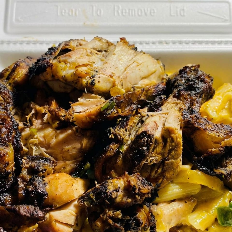 Open takeout container filled with grilled chicken, charred meat pieces, roasted potatoes, and yellow-green vegetables.