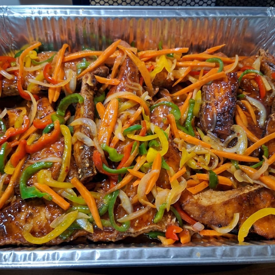 Aluminum catering tray filled with glazed grilled meat topped with sliced carrots, onions, and colorful bell peppers.